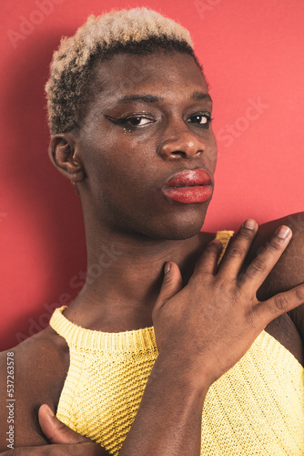 A portrait of an androgynous black guy on a red background. Makeup concept.