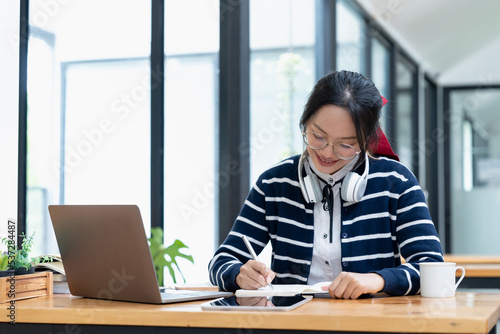 young woman enjoying self-directed learning with online educational tools. Bright student writing in notebook and using laptop computer for e-learning watching webinar or attending e-class