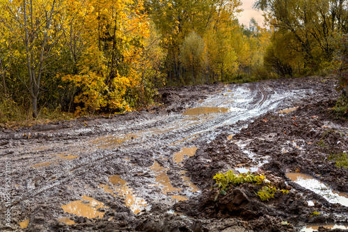 A dirty road impassable from the rain on the background of an autumn landscape.
