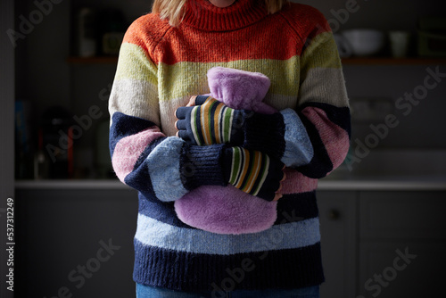 Woman In Gloves Hugging Hot Water Bottle Trying To Keep Warm During Cost Of Living Energy Crisis