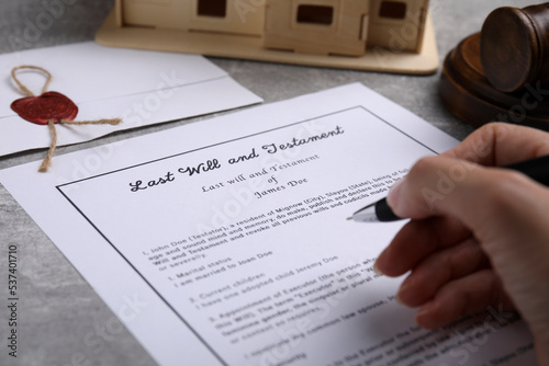 Woman signing last will and testament at light grey table, closeup