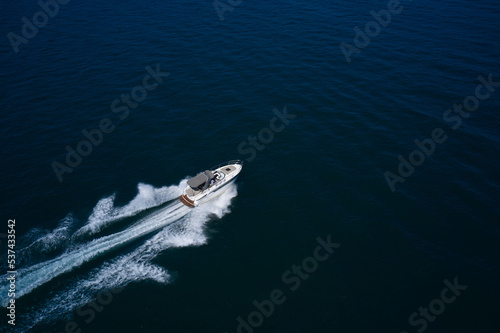 a high-speed big boat with people moves quickly on dark blue water making a white trail behind the boat.