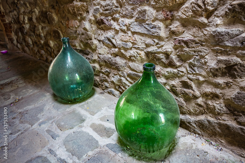 Two big green dusty bottles near stone vintage house wall in the street.