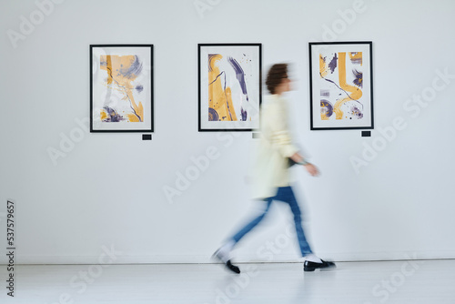 Blurred motion of young woman walking along art gallery with modern art on the wall