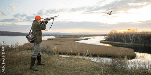  waterfowl hunter shooting into sky during duck hunting at sunrise. hunting banner