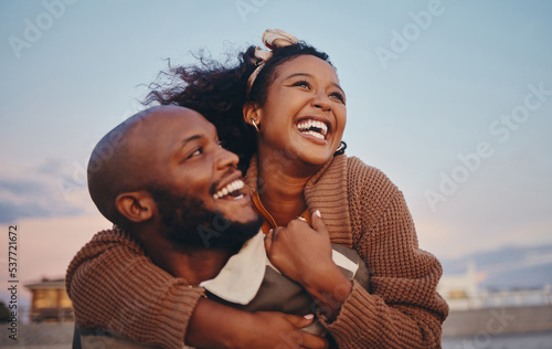 Happy black couple, love and hug laughing in joyful happiness for bonding time together in the outdoors. African American man and woman enjoying playful fun piggyback with smile for holiday in nature