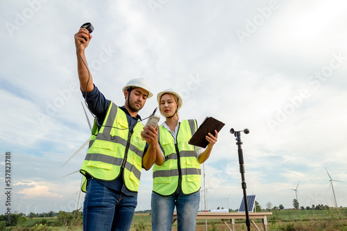 Young engineers team use an anemometer to measure wind speed, temperature and humidity on a wind farm background