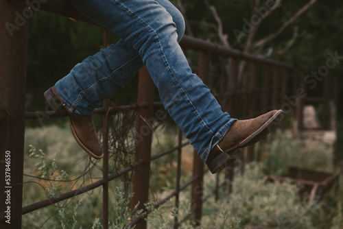 Western lifestyle concept with person sitting on fence in cowboy boots.