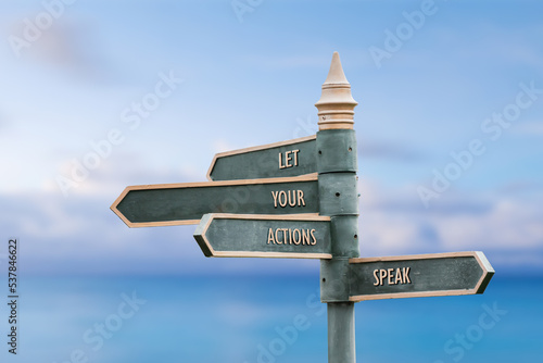 let your actions speak four word quote written on fancy steel signpost outdoors by the sea. Soft Blue ocean bokeh background.