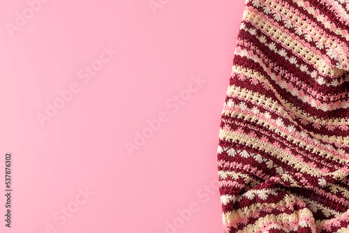 Top view of colorful handmade crochet blanket on pastel pink background with copy space, mockup