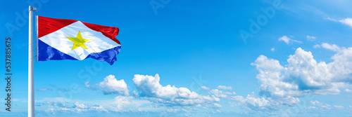 Saba flag waving on a blue sky in beautiful clouds - Horizontal banner