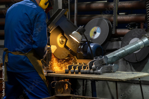 Metal shop factory worker cutting steel with electric grinder tool. Stationary electric circular cutter instrument cuts metal parts. Sparks flying from metal cutting process.