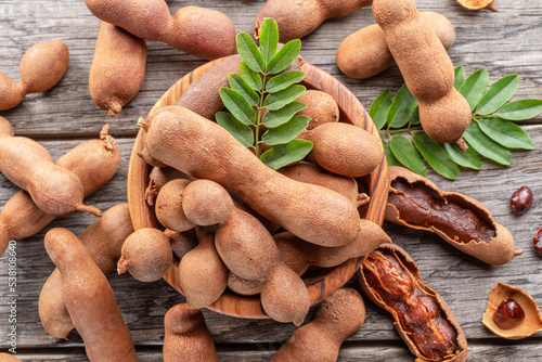 Ripe tamarind fruit, leaves and some tamarind seeds on wooden table.