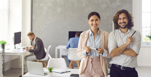 Happy smiling young business people in modern office workplace. Banner background with portrait of two satisfied successful colleagues, team leaders, teammates, business partners and friends at work
