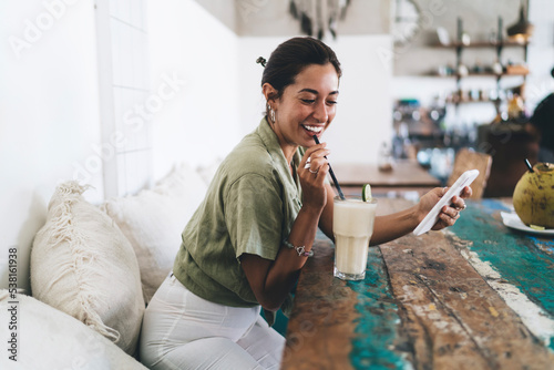 Smiling ethnic woman with milkshake drink and smartphone in cafe