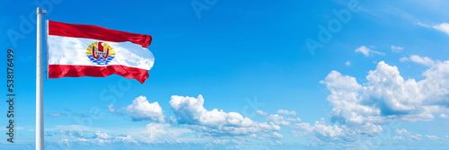 French Polynesia flag waving on a blue sky in beautiful clouds - Horizontal banner
