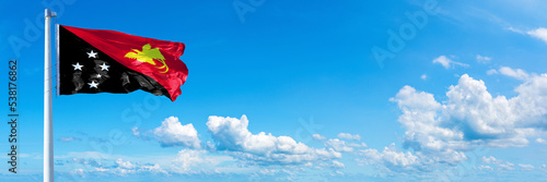Papua New Guinea flag waving on a blue sky in beautiful clouds - Horizontal banner