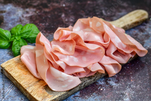 Slices Of Traditional Italian antipasti mortadella Bolognese on a wooden cutting board.