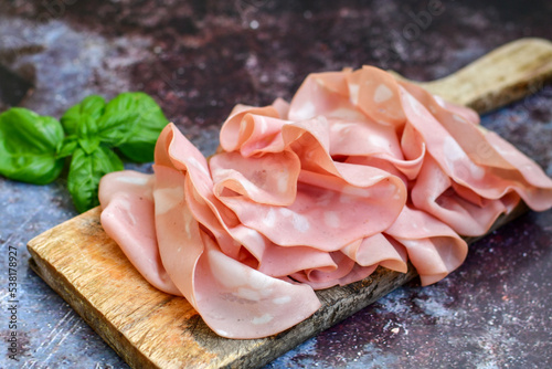 Slices Of Traditional Italian antipasti mortadella Bolognese on a wooden cutting board.