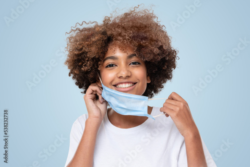 Smiling african american school girl removing face mask after the end of pandemic