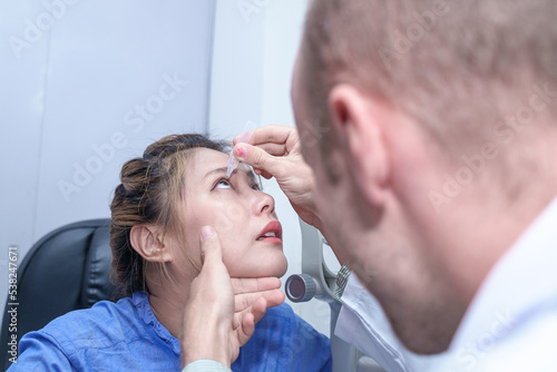 Male doctor ophthalmologists dripping eye drops on eyes of a female patient during a treatment at the ophthalmological office