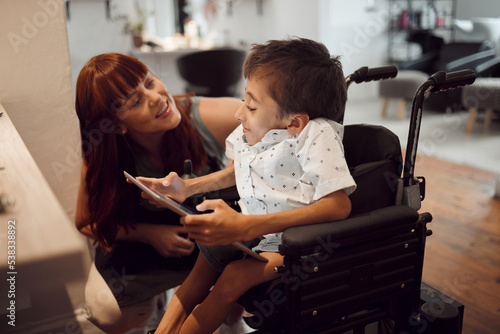 Woman, child disability and tablet, wheelchair friendly and inclusivity, special needs and support. Cerebral palsy and handicap kid, screen time and games, disabled in hairdresser salon.