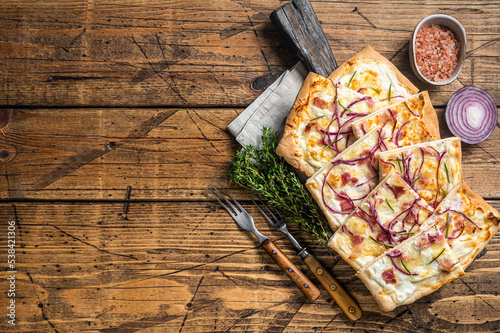 Flammkuchen or tarte flambee with cream cheese, bacon and onions. Wooden background. Top view. Copy space