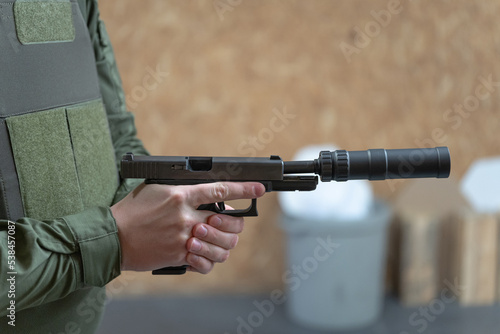 A military man has a pistol with a silencer in his hand, close-up photo.