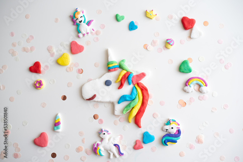 Handmade from color dough shape of unicorn, rainbow, colorful hearts and confetti for decorate cake on white background. Birthday party for child