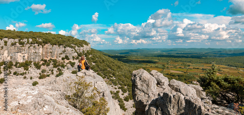 A woman with a backpack sitting on a mountain peak looking at view of languedoc landscape panorama- tourism in France concept