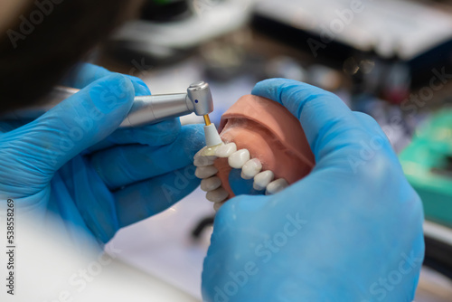 Professional dental technician or dentist holding motor handpiece tool and working with dental prosthesis, tooth dentures - close up view. Stomatology, medicine, restoration concept