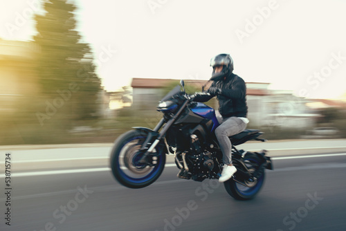 Side view of a motorcycle rider riding race motorcycle on a wheelie the highway with motion blur.