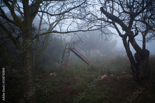 Parque infantil desolado y abandonado cubierto de niebla al anochecer 