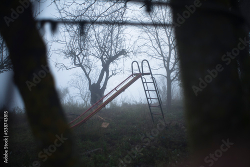 Parque infantil desolado y abandonado cubierto de niebla al anochecer