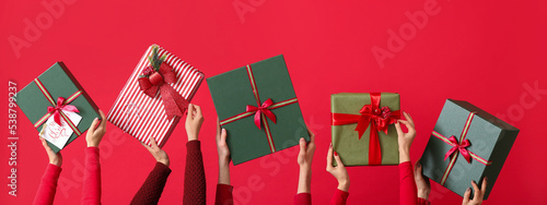 Many hands with Christmas gifts on red background