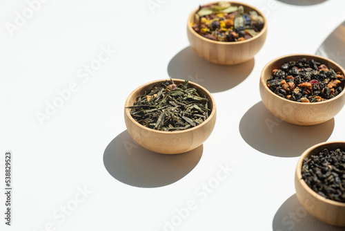 Different types of green, black and herbal tea in a wooden bowl. Variety of dry leaves and flowers. Organic high-quality ingredients for a drink. Soft focus on one bowl