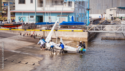 Young people pull a small sailing boat out of the water to shore.