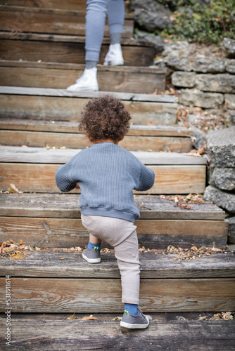 Biracial toddler walking up outdoor steps in backyard garden during fall 