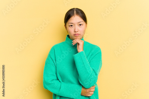 Young Asian woman isolated on yellow background suspicious, uncertain, examining you.