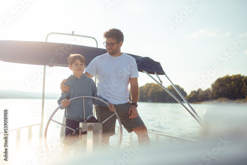 Father and son together steer a ship sailing on a river