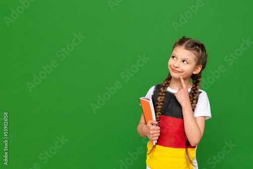 A little girl with a German flag on her T-shirt looks at your advertisement on a green isolated background. German language courses for schoolchildren. Copy space.