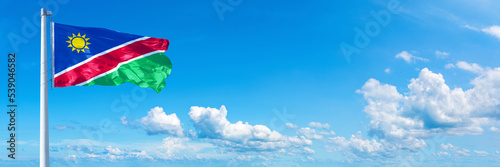 Namibia flag waving on a blue sky in beautiful clouds - Horizontal banner 