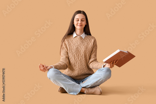 Beautiful woman with book meditating on beige background