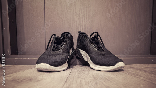 Pair of old black dirty sneakers stands on wooden threshold