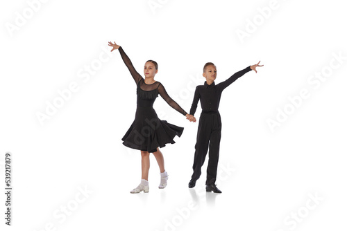 Cha cha cha, rumba, tango. Two kids, school age girl and boy in black stage costumes dancing ballroom dance isolated on white background. Motion, action, hobbies