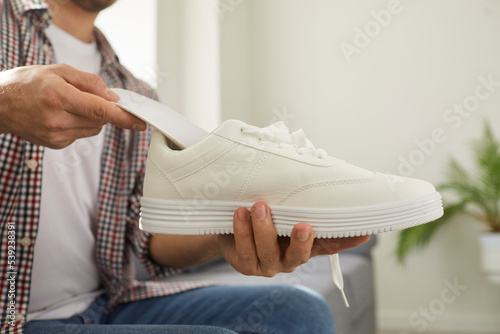 Young man puts clean orthotic insole inside his modern white comfortable orthopedic shoe that he is holding in his hand. Cropped shot. Foot arch support, pain treatment and flatfoot prevention concept