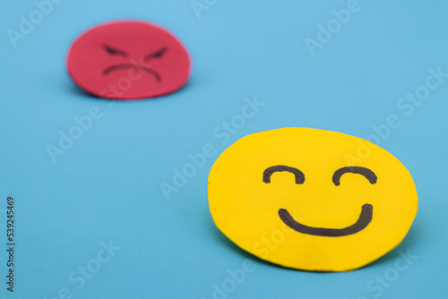 Yellow cut out paper smiley face with another red angry face in the background. concept of envy, selfishness, happiness or well-being