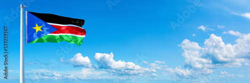 South Sudan flag waving on a blue sky in beautiful clouds - Horizontal banner