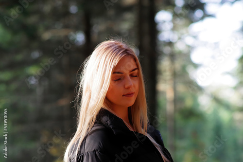 Blond kobieta w lesie jesienią z zamkniętymi oczami.