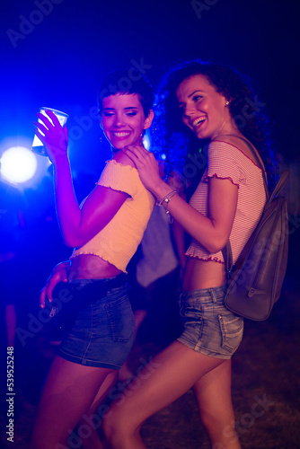 Two happy young girls dancing and drinking beer on the party concert in the night club 